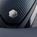 Charles Owen Hyda Carbon riding hat in Navy Matte/Navy Gloss, close-up of the brushed metal crown badge and peak